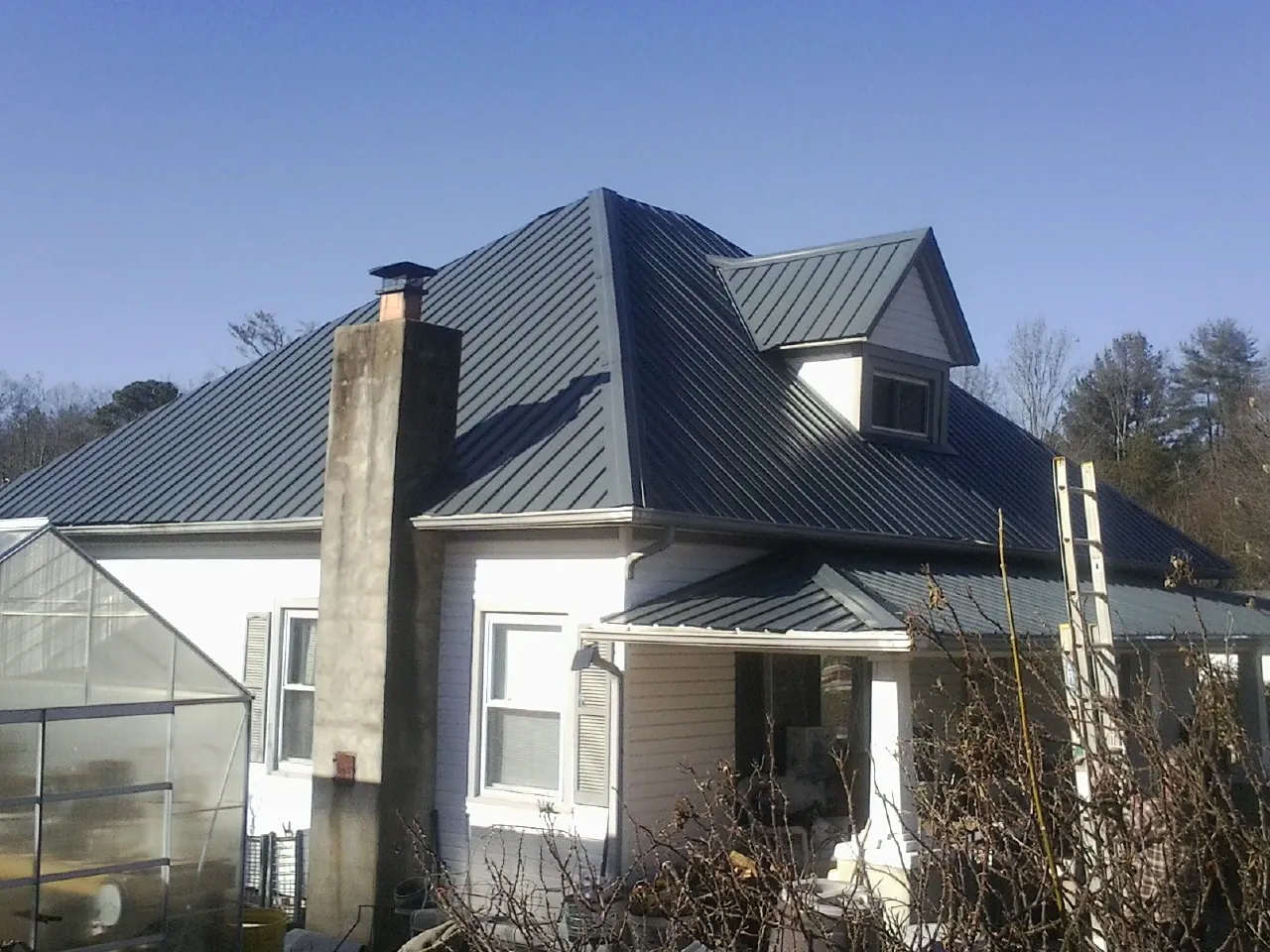 Dark blue standing seam metal roof on a white farmhouse with dormer — Slate & Tile Roof Repair by Roofing Brothers in Spring Valley