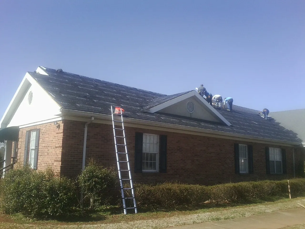 Crew tearing shingles off a brick ranch roof with a ladder set — Emergency Roof Repair work by our crew in Spring Valley